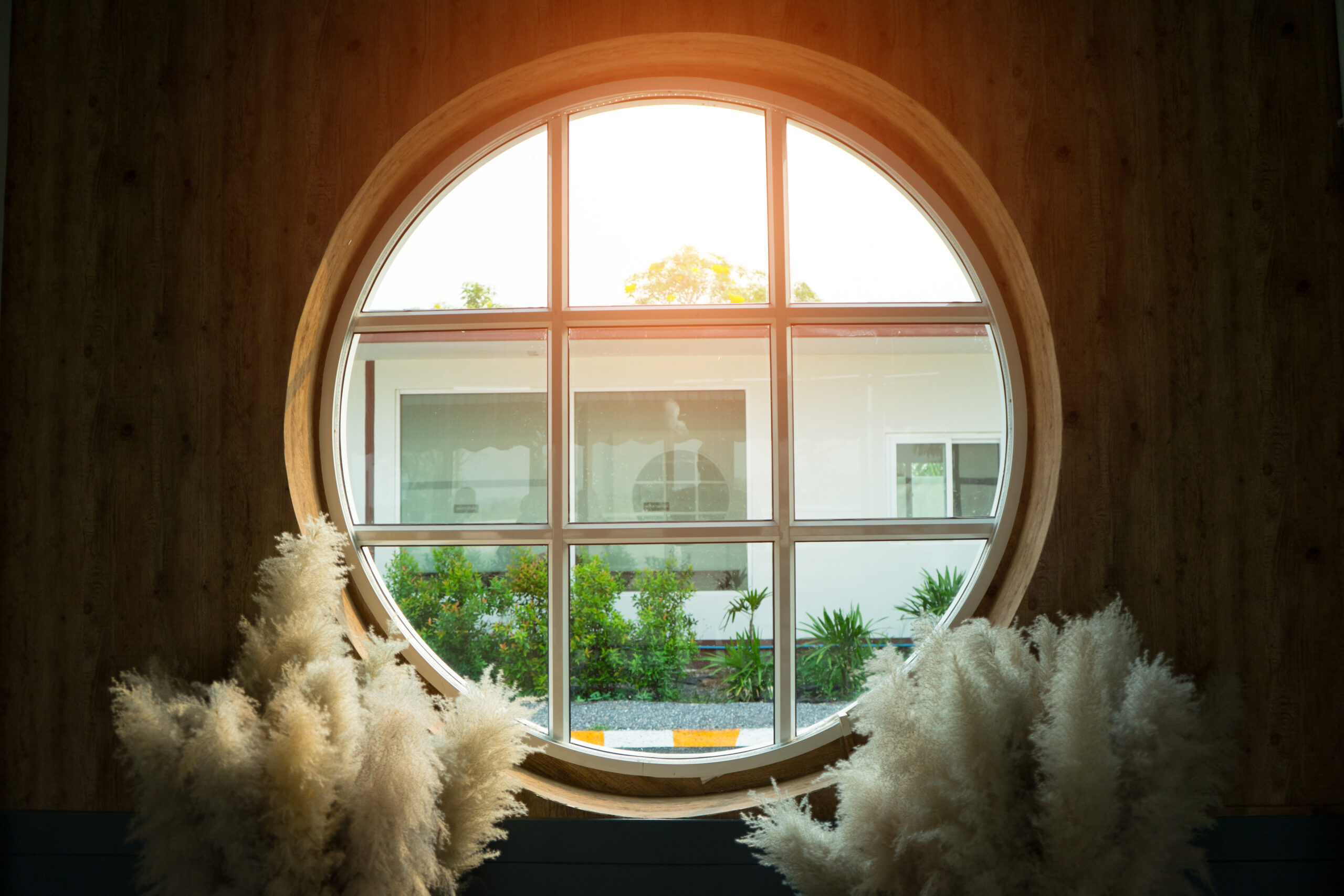 The glass circle window for to see view outside the house with white flower grass near it and sunlight to shine in.