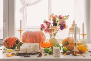 Various pumpkins, candles and a bouquet in a vase on the windowsill. Autumn decorations.