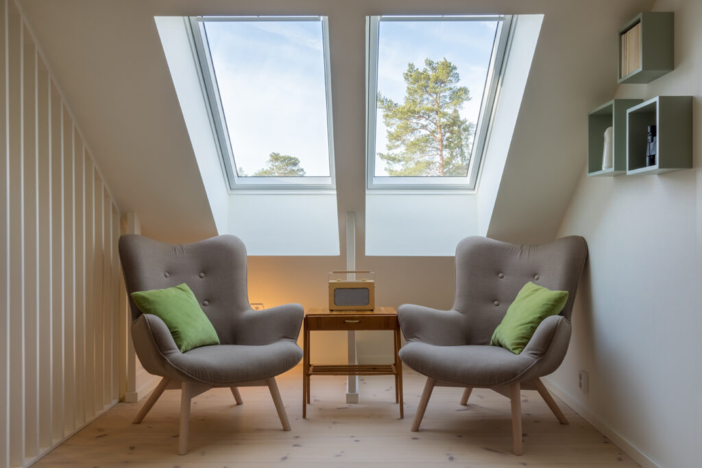 Modern retro design in a attic / loft. Small vintage table with a radio on and two reading chairs under two skylights.