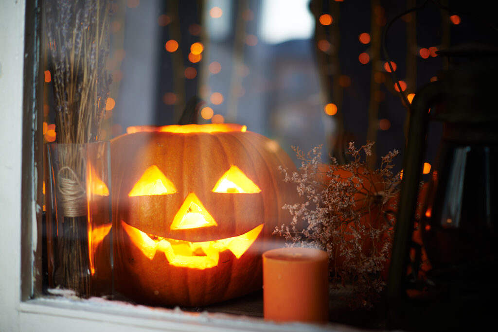 Big pumpkin with burning candle inside in a window with fall and halloween decorations