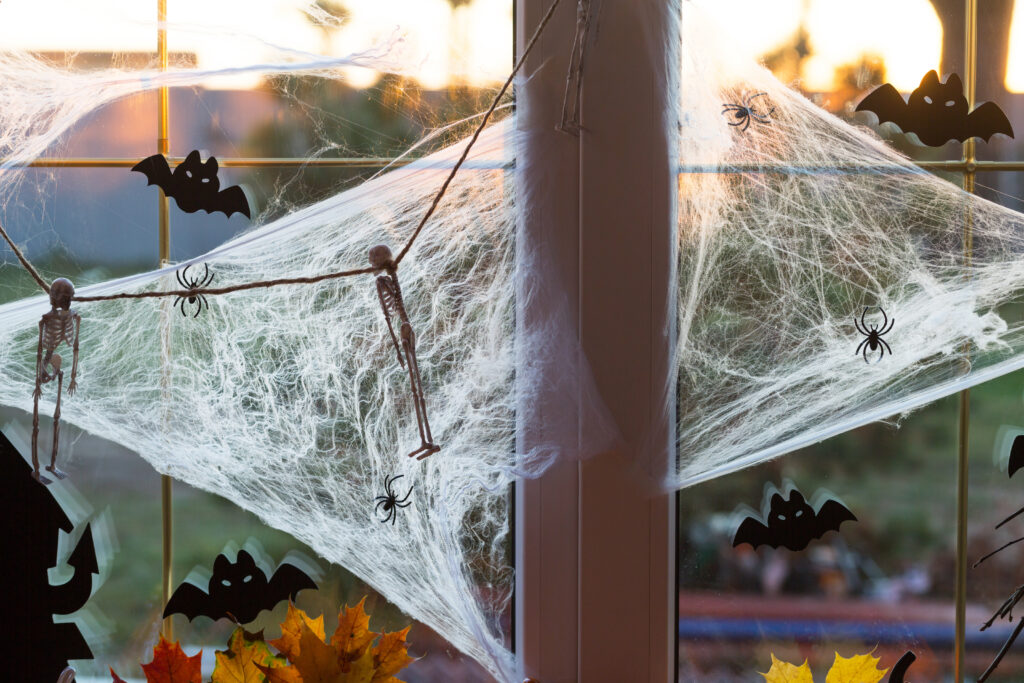 Festive halloween decor in the windowsill. There are pumpkins, Jack o lanterns, skulls, bats, cobwebs, spiders, candles and a garland.