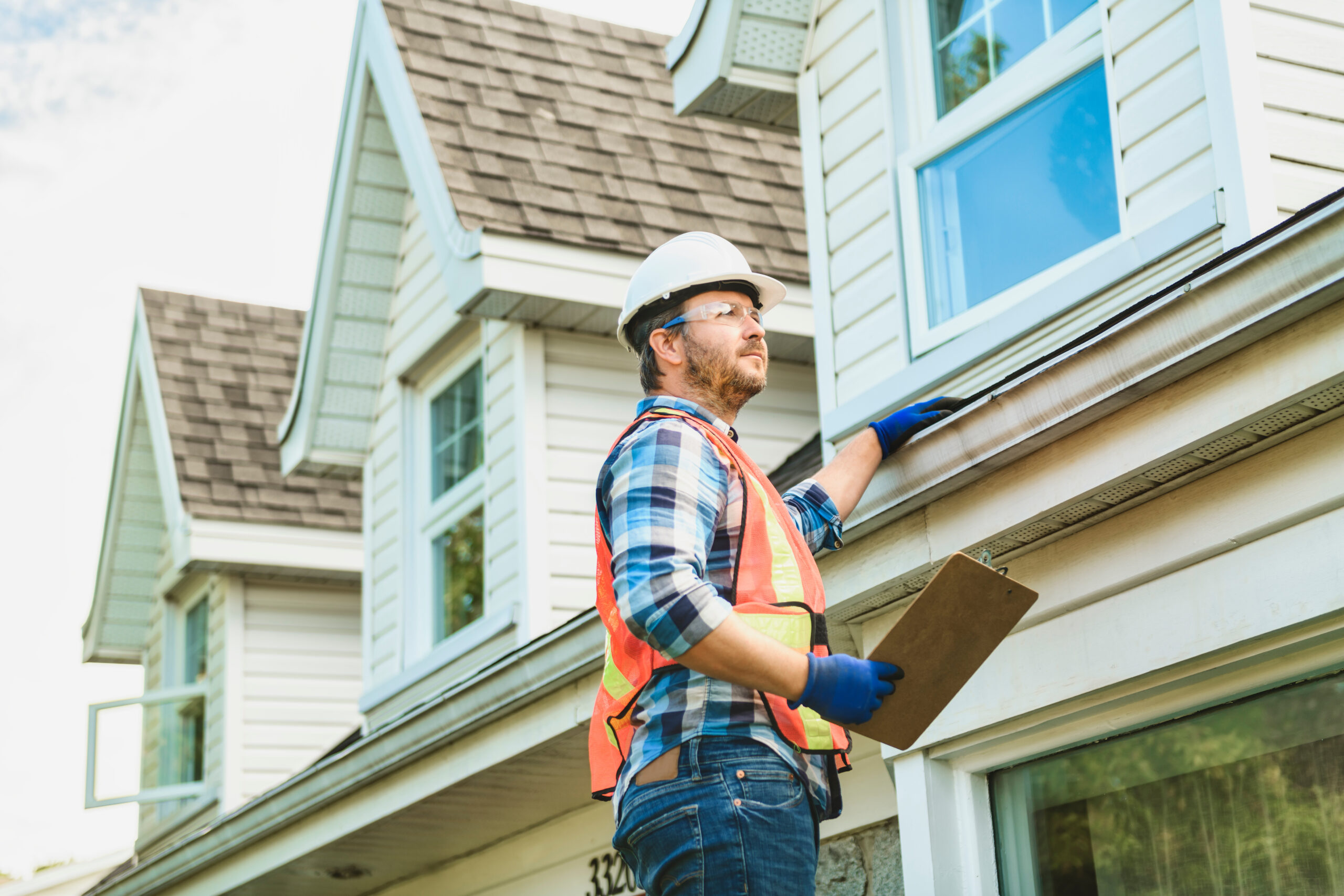 A man with hard hat standing on steps inspecting house roof