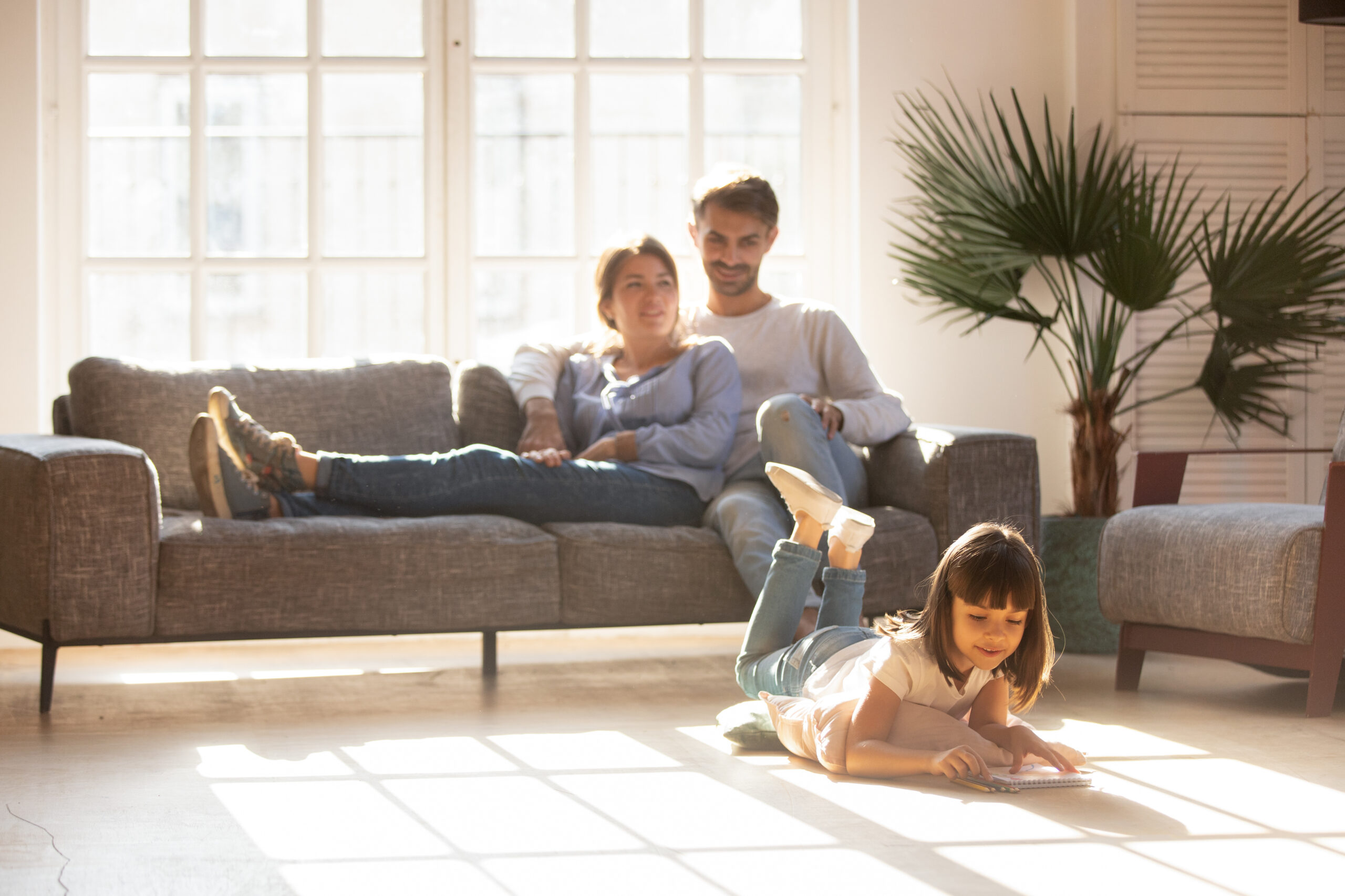 Happy parents relaxing on couch while kid drawing on floor