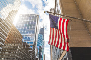 USA flag in Chicago with with skyscrapers on background. American flag waving in the city on a sunny day. Clouds reflections on buildings facade