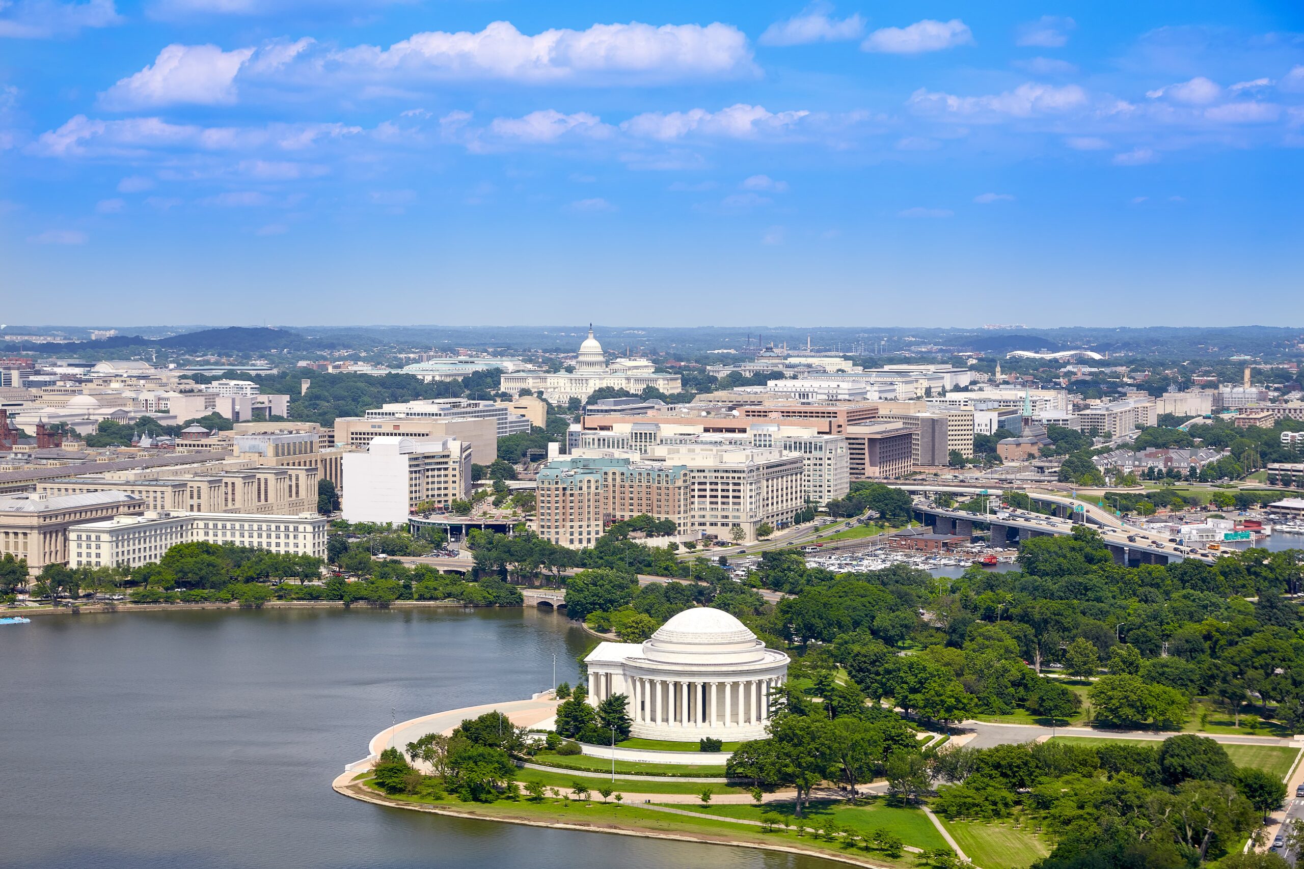 AdobeStock_206977592 An aerial view of Washington D.C. features the Jefferson Memorial in the foreground, a large body of water, and the city skyline with the Capitol Building in the distance under a blue sky