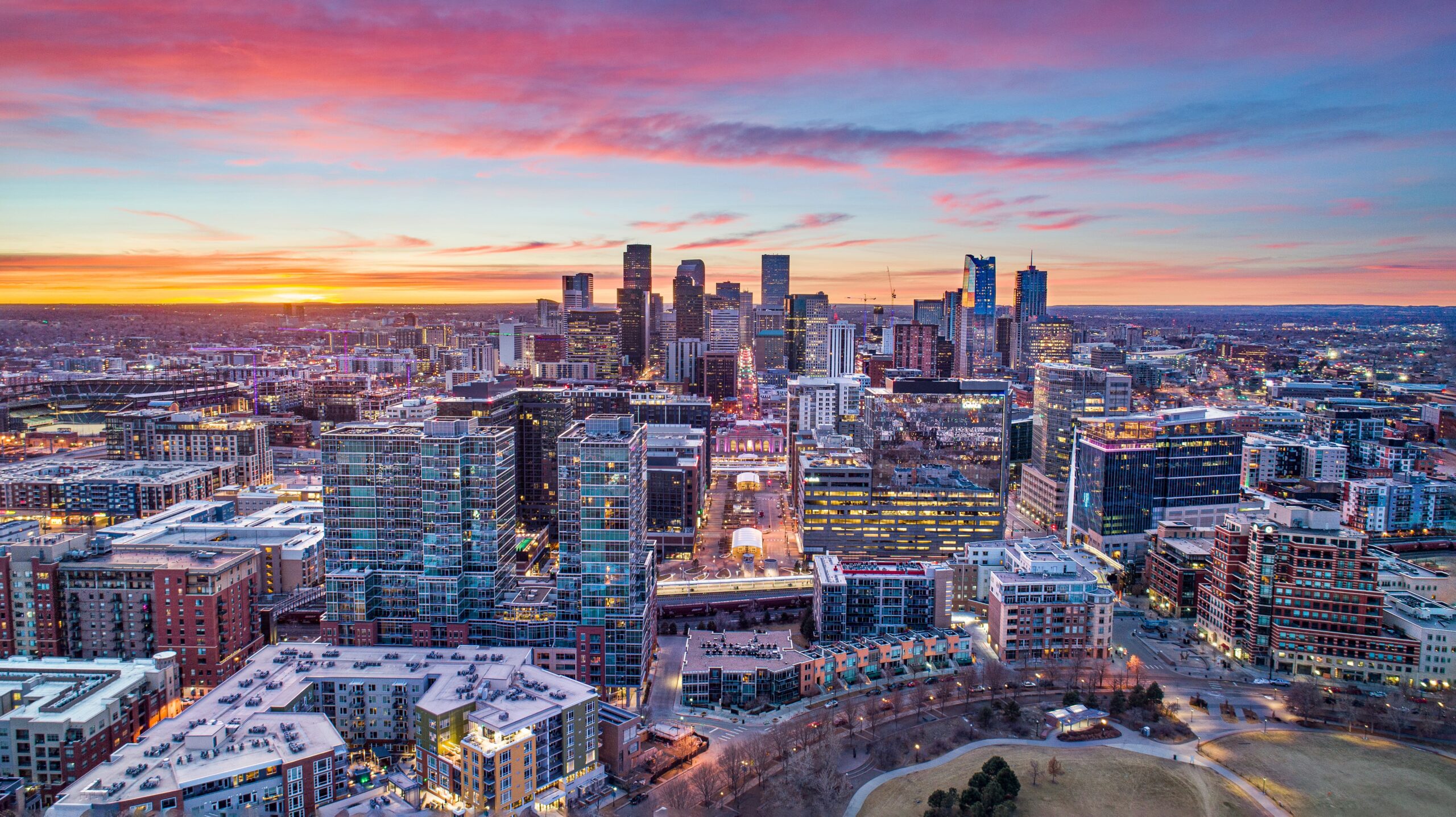 AdobeStock_320873812 An aerial view captures a diverse city landscape with tall buildings, suburban areas, a river, and green spaces under a cloudy sky.