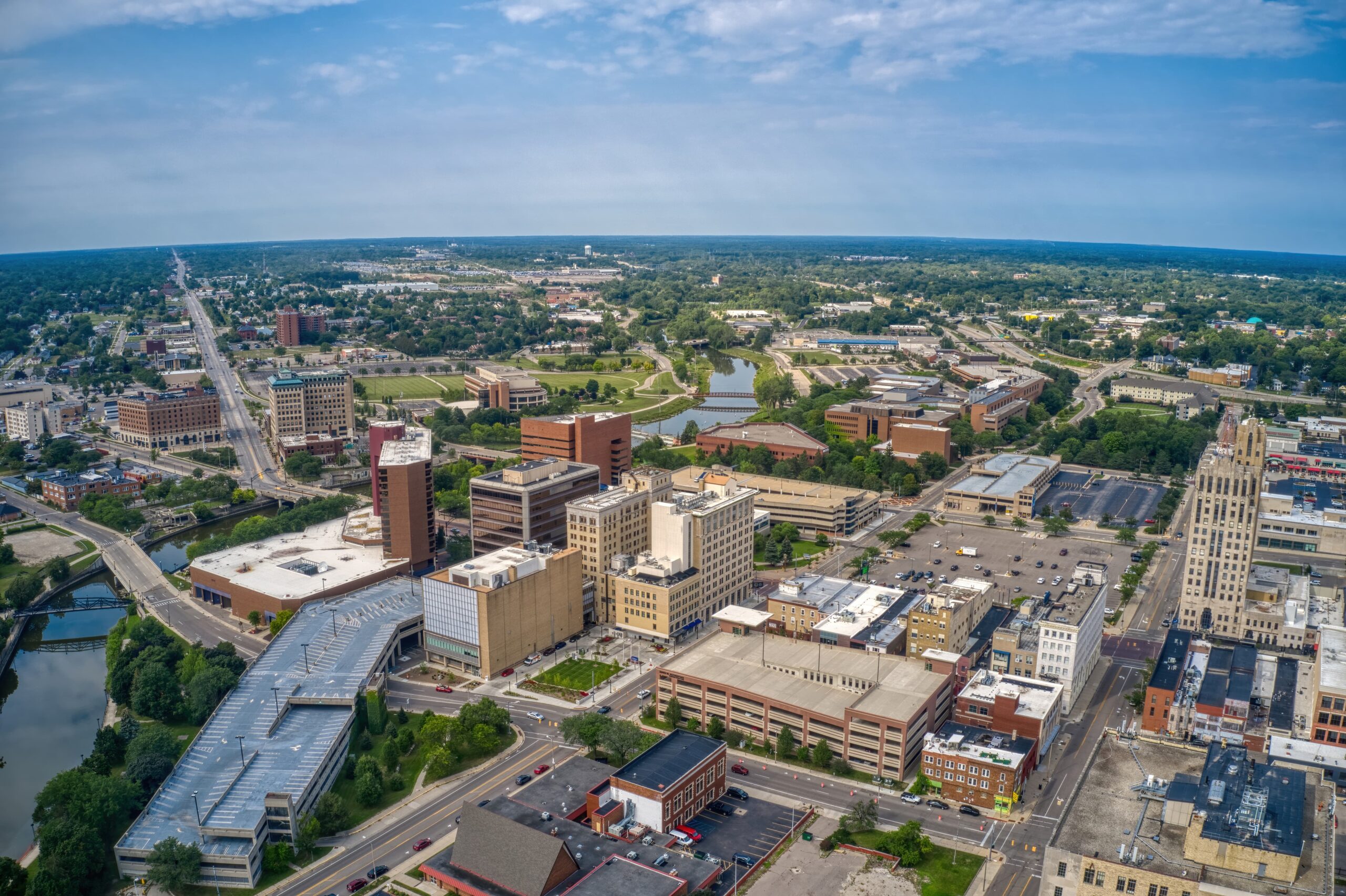 AdobeStock_448838380 An elevated view showcases a city skyline with various buildings, a curving railway, and parked cars under a bright blue sky