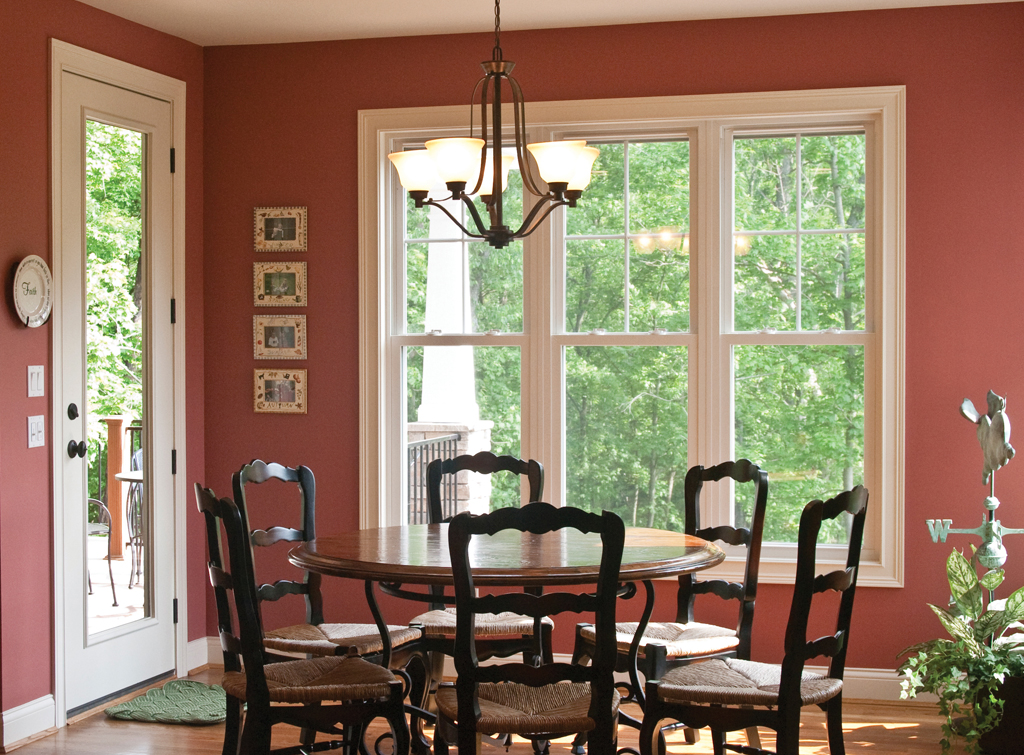 a dining room with three windows and a that open the view up to the foliage in the yard outside